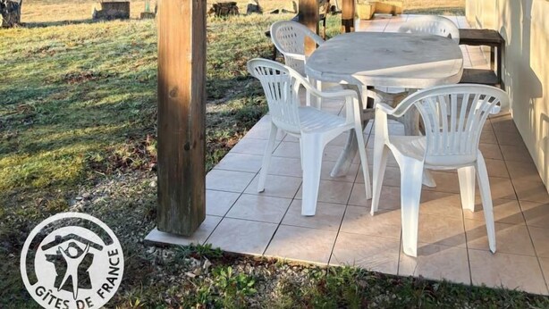 Ein überdachter Patio-Bereich mit einer Holzkpergola, einem runden Tisch und vier weißen Plastikstühlen.
