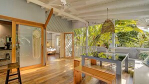 Un salón amplio con suelo de madera, un separador de vidrio y vistas a abundante vegetación a través de un ventanal grande.