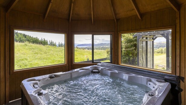 Een hottub in een houten chalet met grote ramen, met uitzicht op een grasachtig landschap.