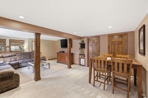 Un salón espacioso con un sofá grande, una mesa de comedor con sillas, un aparador de madera y un televisor montado en la pared.
