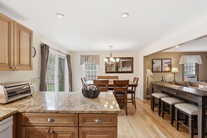 Una cocina con encimera de granito, armarios de madera, una zona de comedor con mesa y sillas, y una barra con taburetes.
