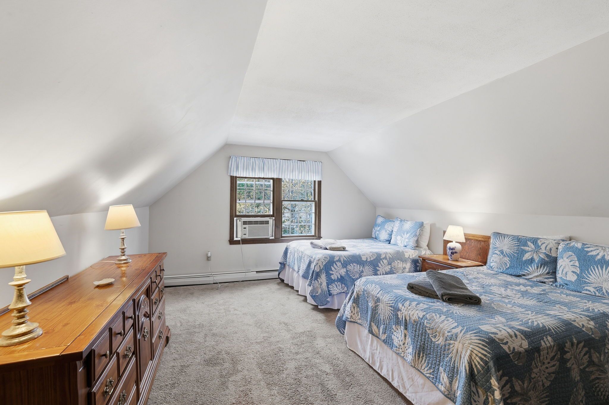 A bedroom with two beds, a dresser, lamps, and a window.