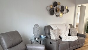 A modern living room with a grey sofa, a grey armchair, and a glass coffee table. - Farmhouse in the Heart of DowntownAuburn Hills (Auburn Hills)