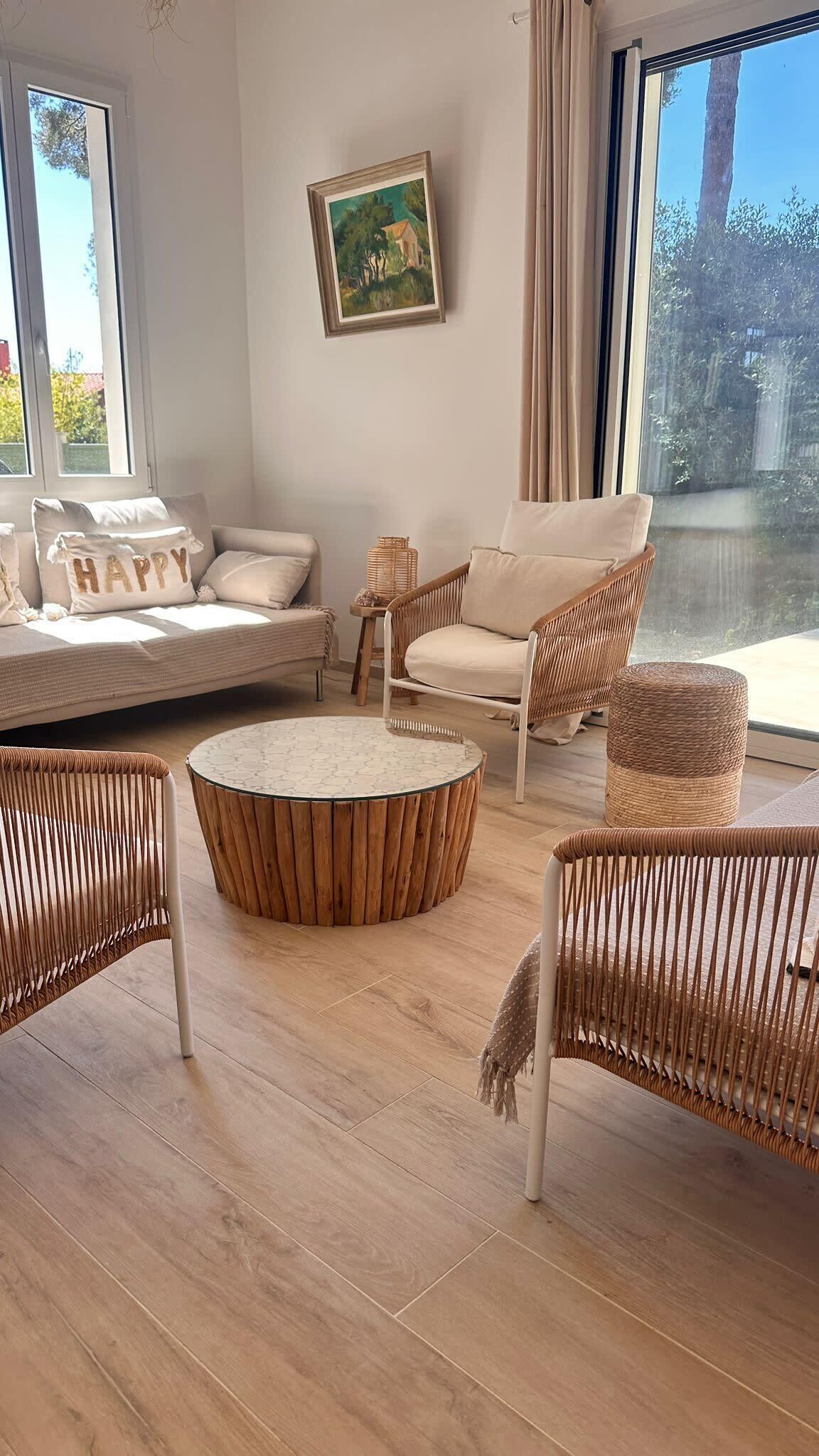 Un salon moderne avec un ensemble de canapés, des fauteuils en osier, une table basse ronde et un tableau accroché au mur.