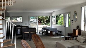 A spacious living area with a high ceiling, a dining table, a sofa, and a wicker chair. - Dedans-dehors - 10 min from the beach, wifi, air conditionated (Bormes-les-Mimosas)