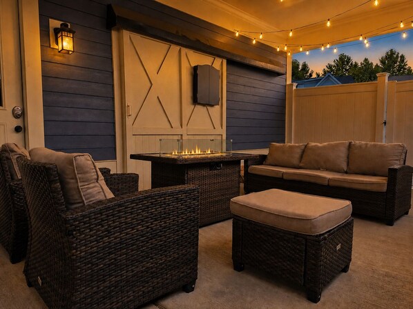 An outdoor seating area with wicker furniture, a fire feature, and string lights.