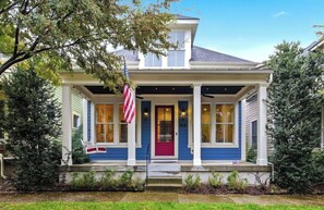 Een huis met twee verdiepingen, een veranda, een rode deur en een Amerikaanse vlag.