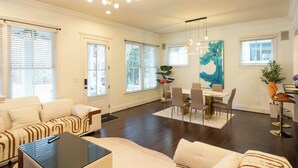 Un salón amplio con un sofá grande, una zona de comedor con una mesa y sillas, y una cocina con una planta y un florero.