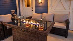 A glass-top table with two glasses and a fire feature, surrounded by wicker furniture and a blue wall.