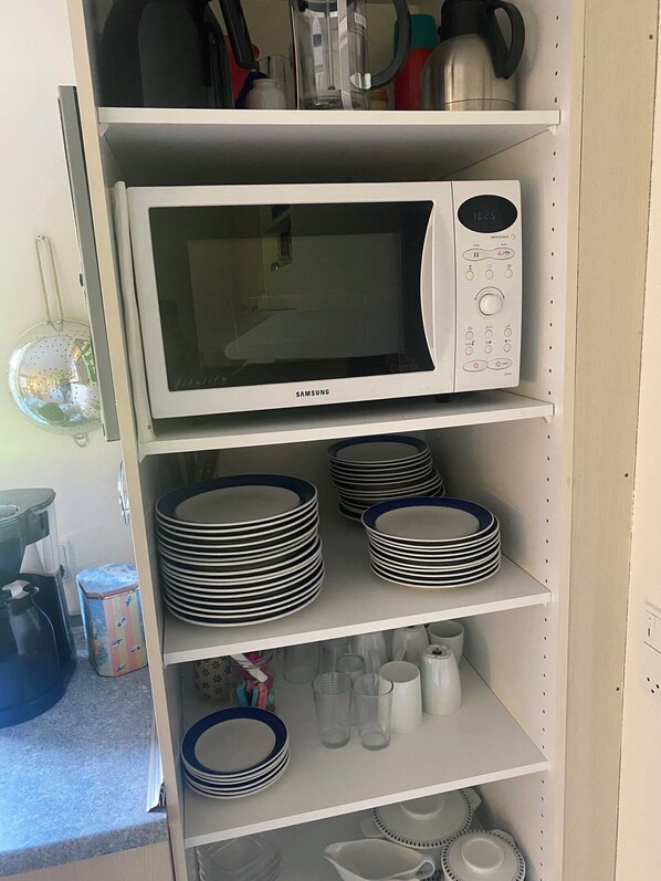 Une cuisine équipée d’un four à micro-ondes, avec des assiettes et des tasses empilées sur des étagères.
