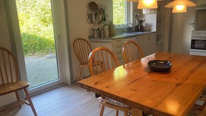 A dining area with a wooden table, chairs, and a kitchen in the background. - Holiday house – located in a forest area (Glesborg)