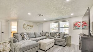 Ein geräumiges Wohnzimmer mit einem grauen Ecksofa, einem kleinen runden Tisch und einem Flachbildfernseher.