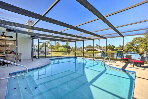 An indoor swimming pool with a glass ceiling, surrounded by lounge chairs and a dining area.