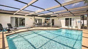 Área de piscina com teto de vidro, espreguiçadeiras e um terraço com mesa e cadeiras.