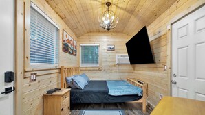 A wooden cabin bedroom with a bed, bedside tables, a desk, and a mounted TV. - Immerse in Julian Cozy Cabin w Fireplace & Deck (Julian)