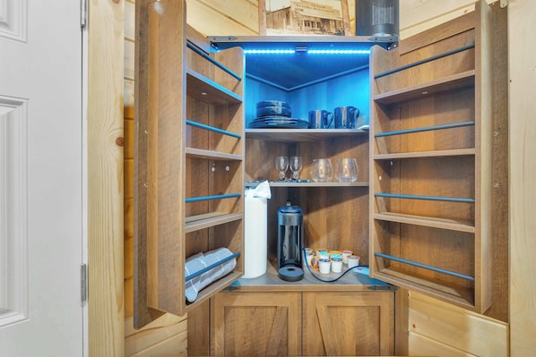 A wooden cabinet with shelves, a coffee maker, and a bottle of hand sanitizer.