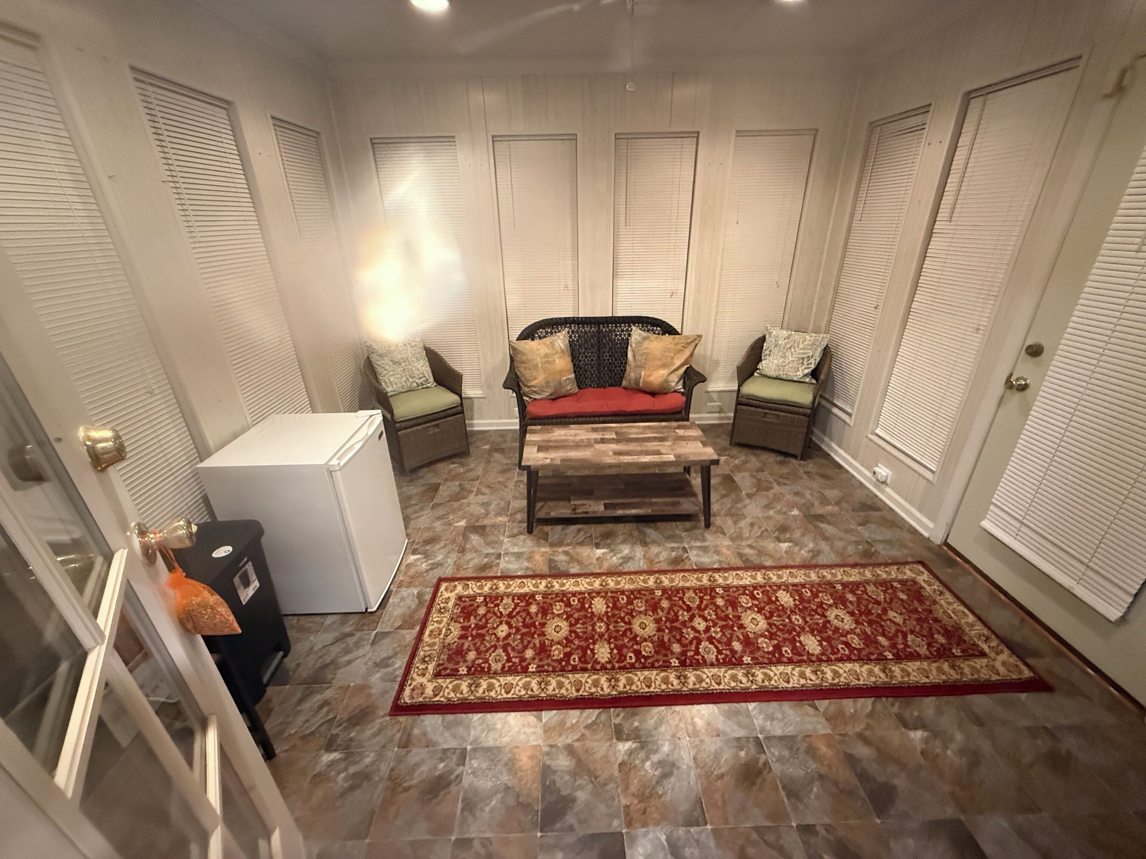 A compact living space with a sofa, two chairs, a coffee table, a refrigerator, and a patterned rug.