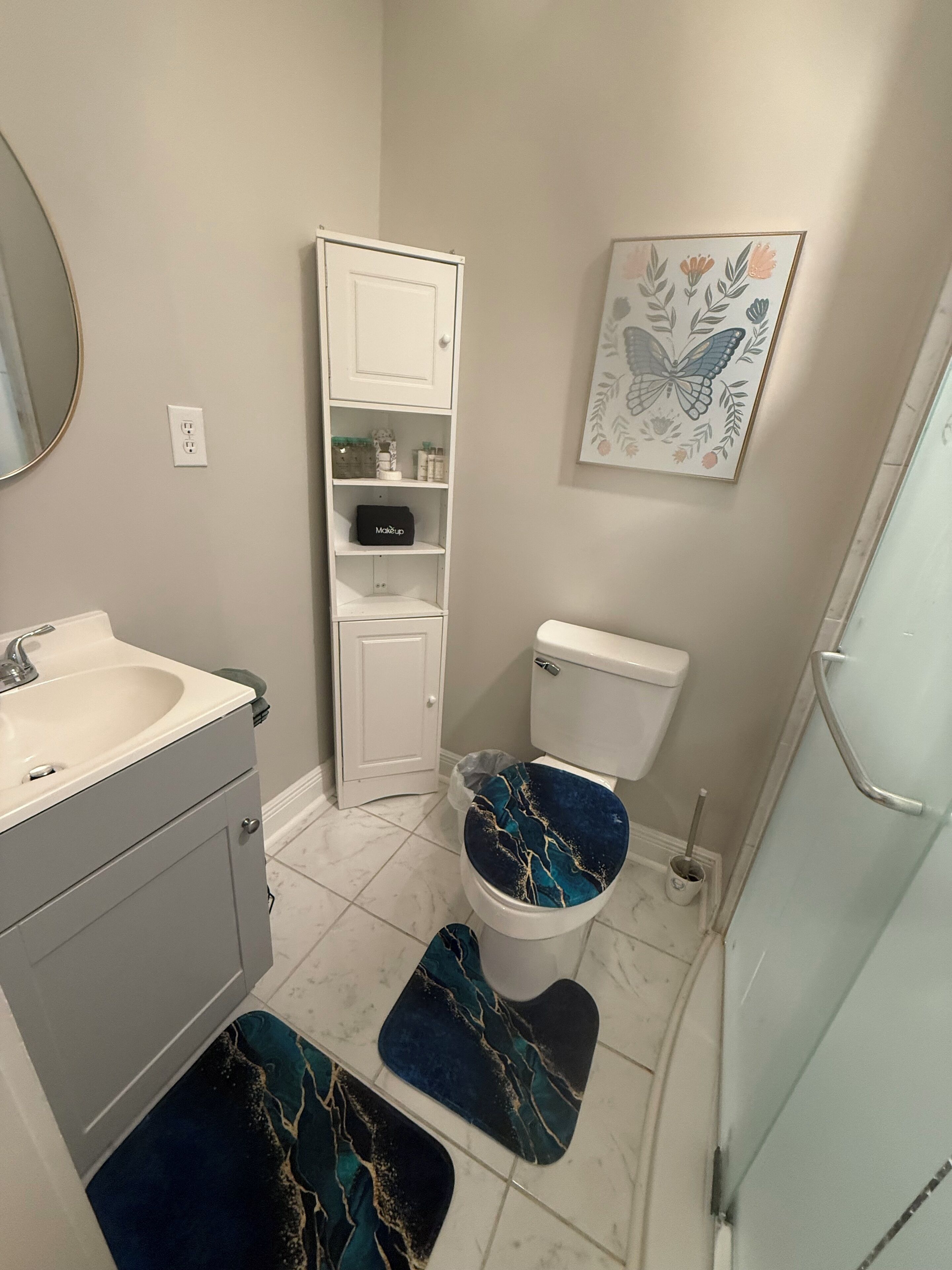 Un bagno con un lavandino bianco, uno scafo per WC azzurro, uno scaffale per cosmetici e un quadro con fiori appeso al muro.