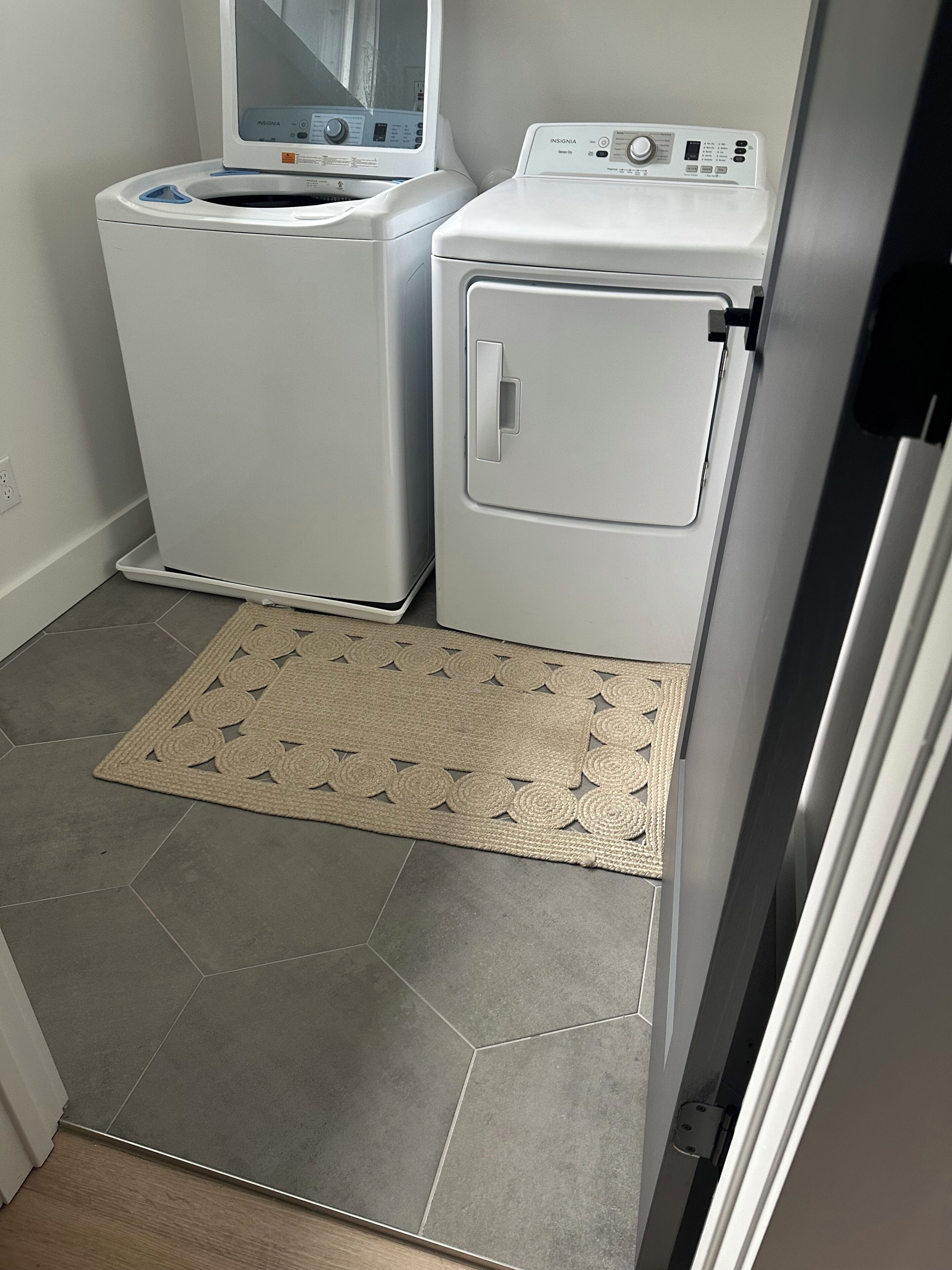 A laundry room with two white washing machines and a beige woven mat on the floor.