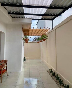 A covered corridor with tiled flooring, potted plants, and a wooden chair. - New Home - Gated+Pool +AC (managua)