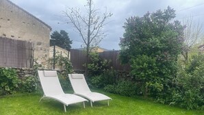 Une cour arrière verdoyante avec deux chaises longues blanches et un mur de pierres.
