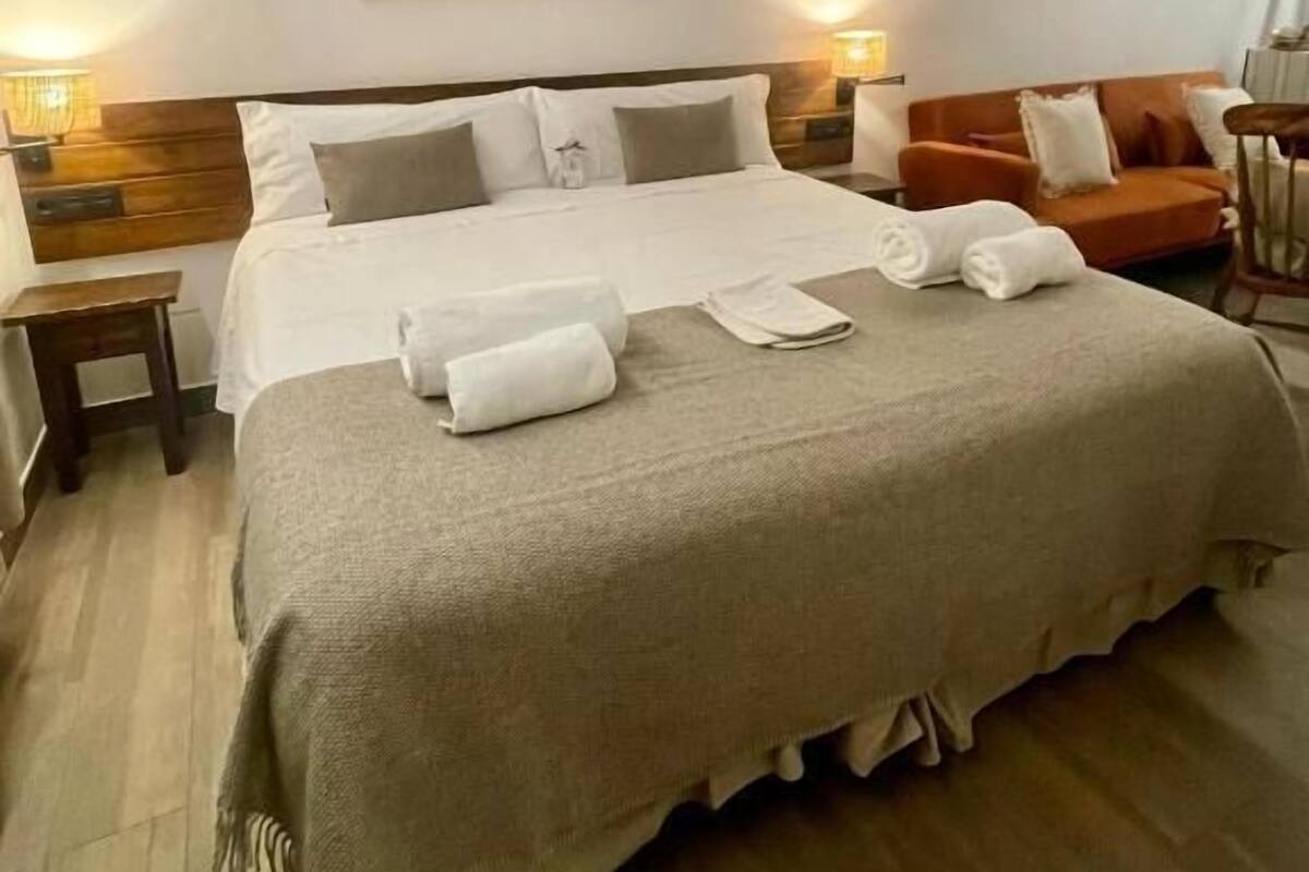 Een goed verlichte slaapkamer met een groot bed, een houten hoofdbord en een hangend kunstwerk erboven.
