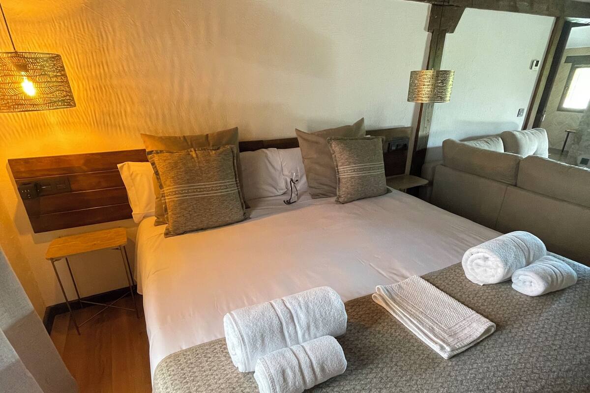 Een net opgemaakt bed met kussens, een nachtkastje, een lamp en uitzicht op de omgeving.