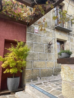 Un edificio de piedra con un muro rojo, un gran árbol en maceta y una rejilla de metal en el suelo.