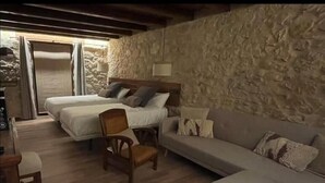 Une pièce chaleureuse avec un mur en pierre, deux lits, un canapé et une chaise en bois.