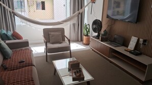 A living room with a hammock, a sofa, a chair, a coffee table, a TV, and a potted plant. - Apartment for 4 people - Spacious and 700m from the beach. (João Pessoa)