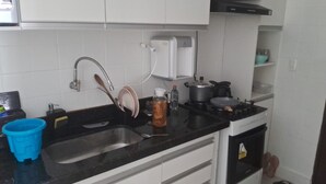 A kitchen with a black countertop, a sink, a stove, and a white cabinet above the sink. - Apartment for 4 people - Spacious and 700m from the beach. (João Pessoa)