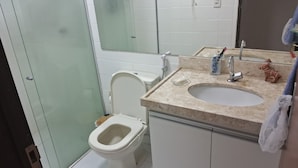 A bathroom with a toilet, a sink, and a mirror. - Apartment for 4 people - Spacious and 700m from the beach. (João Pessoa)