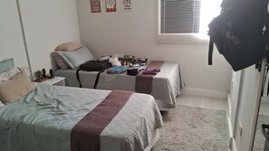 Ein Schlafzimmer mit zwei Betten, einem Fenster mit Jalousien und einem Koffer auf einem Bett.
