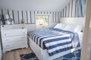 Ein Schlafzimmer mit Bett, Kommode, Fenster und Blick ins Freie.