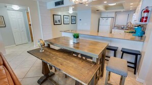 A modern kitchen with a wooden dining table, bar stools, and a small island. - Nice NEW 2BR,Direct Oceanfront in Private Arcadian (Myrtle Beach)