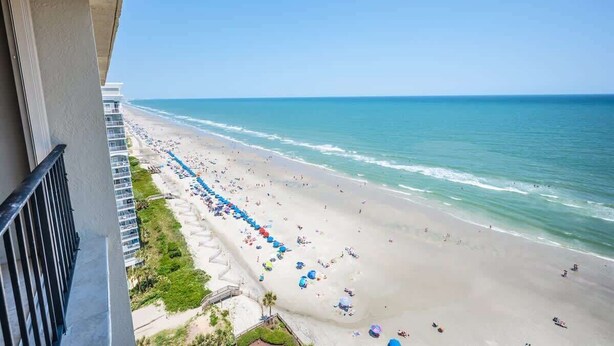 A beach with umbrellas and people, viewed from a balcony. - Nice NEW 2BR,Direct Oceanfront in Private Arcadian (Myrtle Beach)