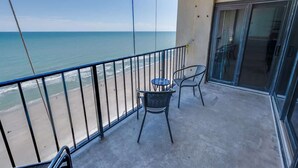 A balcony with a view of the ocean, a table with chairs, and a sliding glass door. - Nice NEW 2BR,Direct Oceanfront in Private Arcadian (Myrtle Beach)