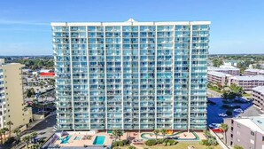 A high-rise hotel with a modern glass facade, multiple balconies, and a pool area with sun loungers. - New Private 4BR Ashworth,  Direct Oceanfront Views (North Myrtle Beach)
