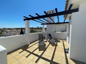 Eine Dachterrasse mit einer Pergola, einem Tisch mit Stühlen und Blick auf die Skyline.