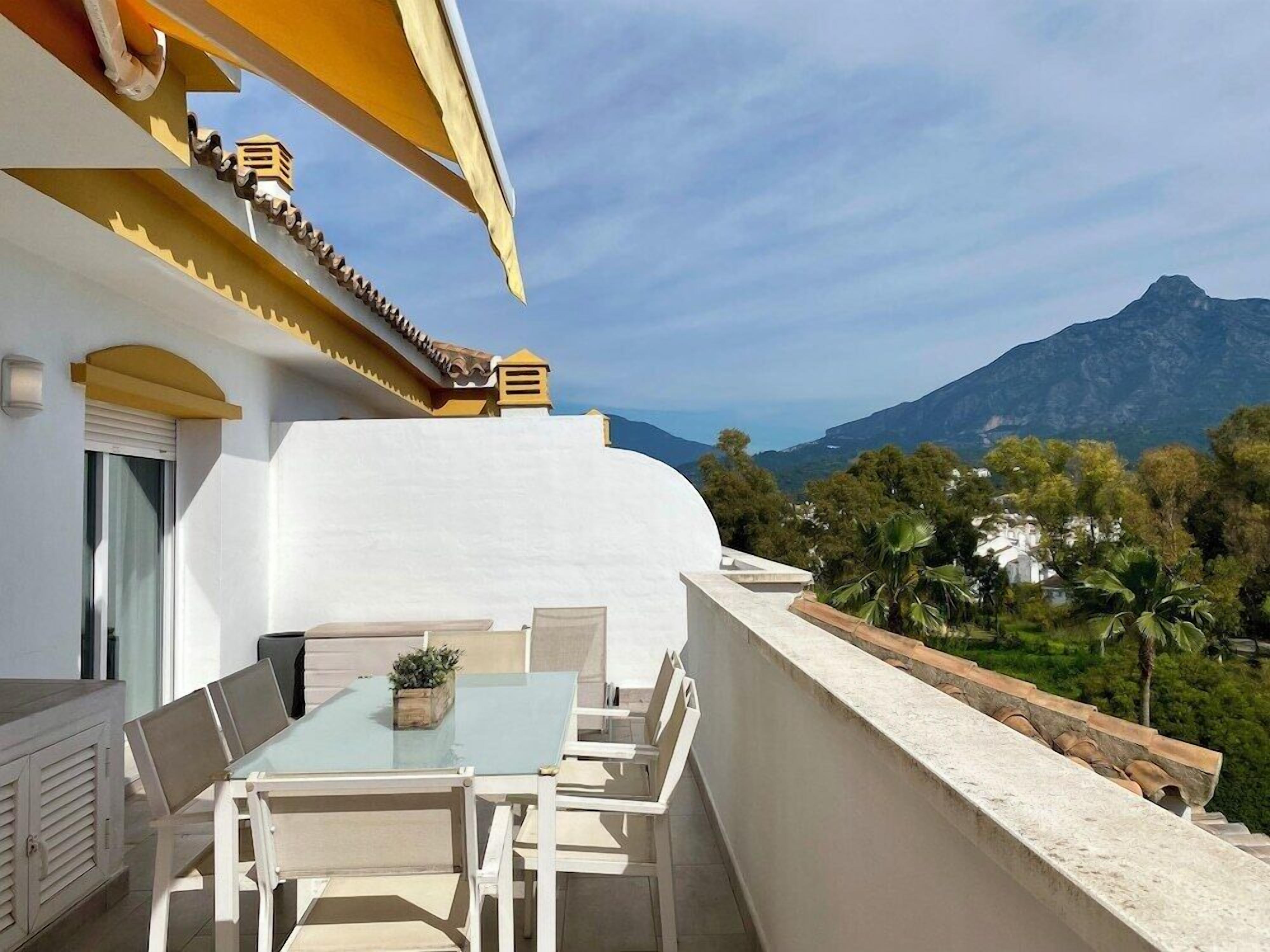 Ein Balkon mit Tisch und Stühlen, der auf eine grüne Berglandschaft blickt.