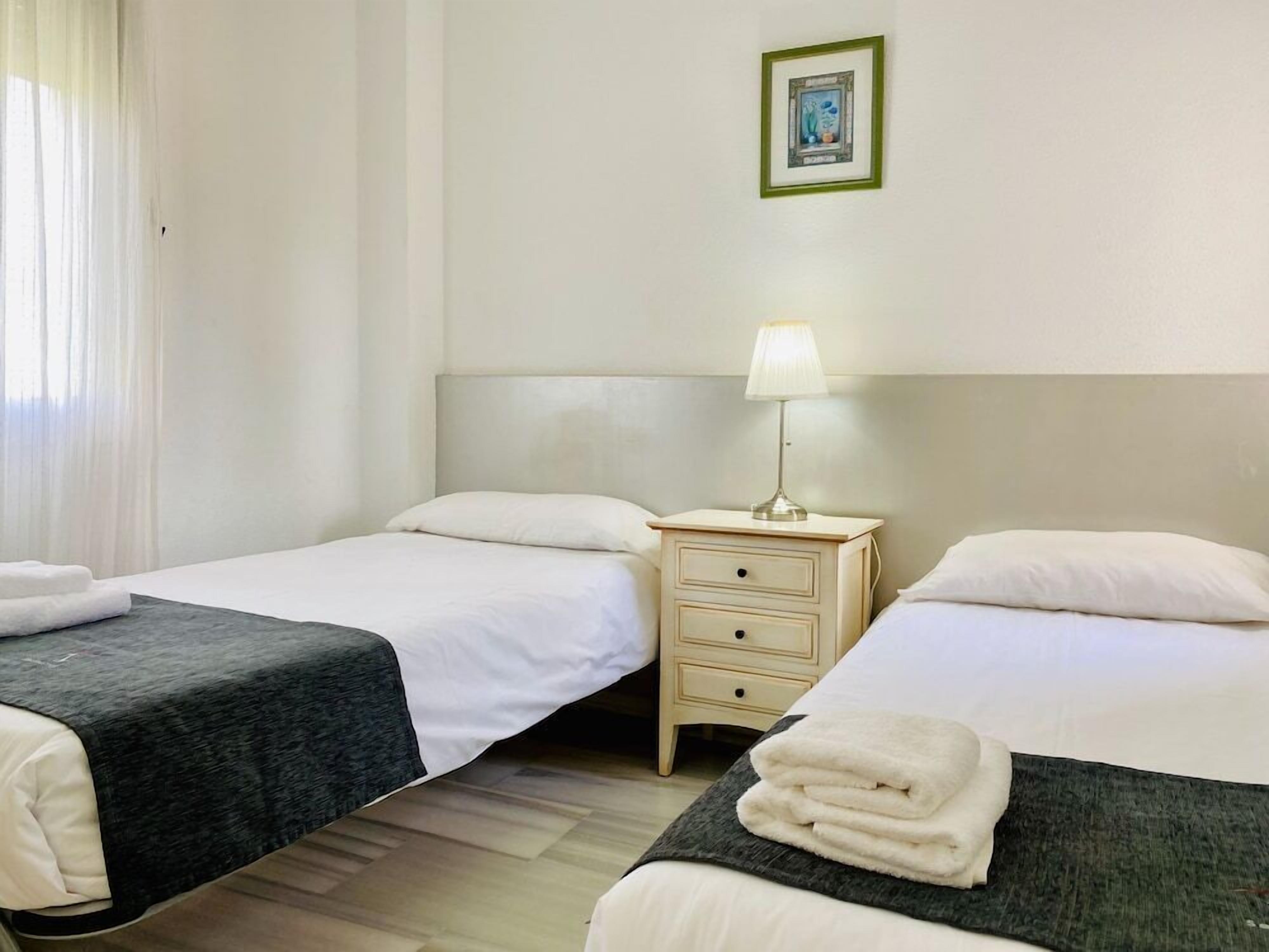 Ein Hotelzimmer mit zwei Betten, einem Nachttisch mit Lampe und einem gerahmten Bild an der Wand.