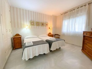 Ett hotellrum med två sängar, en byrå i trä, en stol och ett fönster med gardiner.