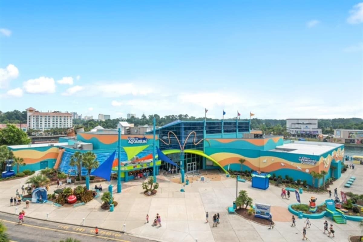 Un espace extérieur avec un grand bâtiment doté d’une façade colorée et d’une enseigne bien visible indiquant la présence d’un aquarium.