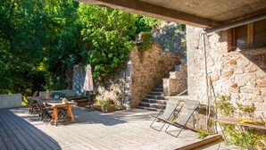 Une terrasse extérieure avec une plateforme en bois, une table et des chaises, et un mur en pierre avec un escalier.