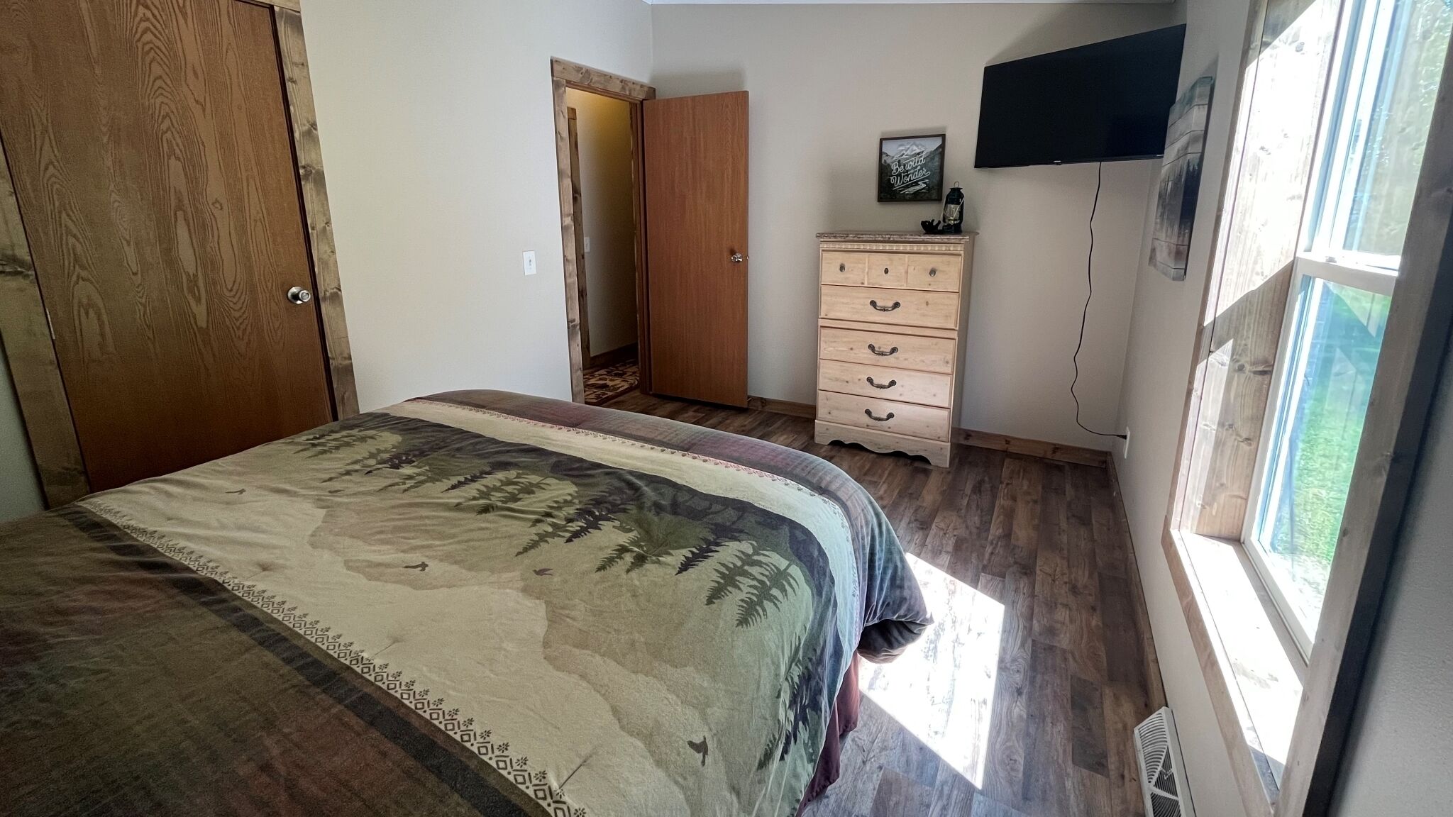 A bedroom with a bed, a dresser, a television, and a window.