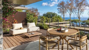 An outdoor patio with a wooden deck, a round wooden table with chairs, a sofa with cushions, and a view of the sea. - Savoy Monumentalis XI – Luxury with sea view (Funchal)