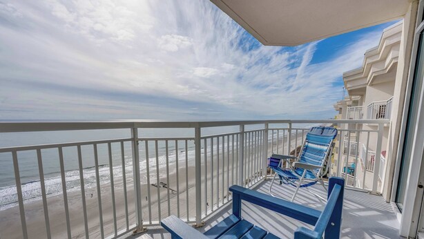 Un balcon avec vue sur la plage, une balustrade et quelques chaises longues.