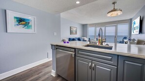 Une cuisine moderne équipée d’un lave-vaisselle, d’un évier et d’un plan de travail. Un tableau encadré est accroché au mur, ainsi qu’une enseigne indiquant « Big Fish Rentals ».