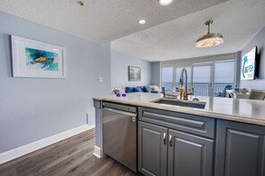 Une cuisine moderne équipée d’un lave-vaisselle, d’un évier et d’un plan de travail. Un tableau encadré est accroché au mur, ainsi qu’une enseigne indiquant « Big Fish Rentals ».
