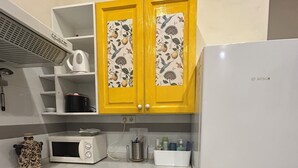 Een keuken met gele kastjes, een witte koelkast, een magnetron, een fornuis en een spoelbak.
